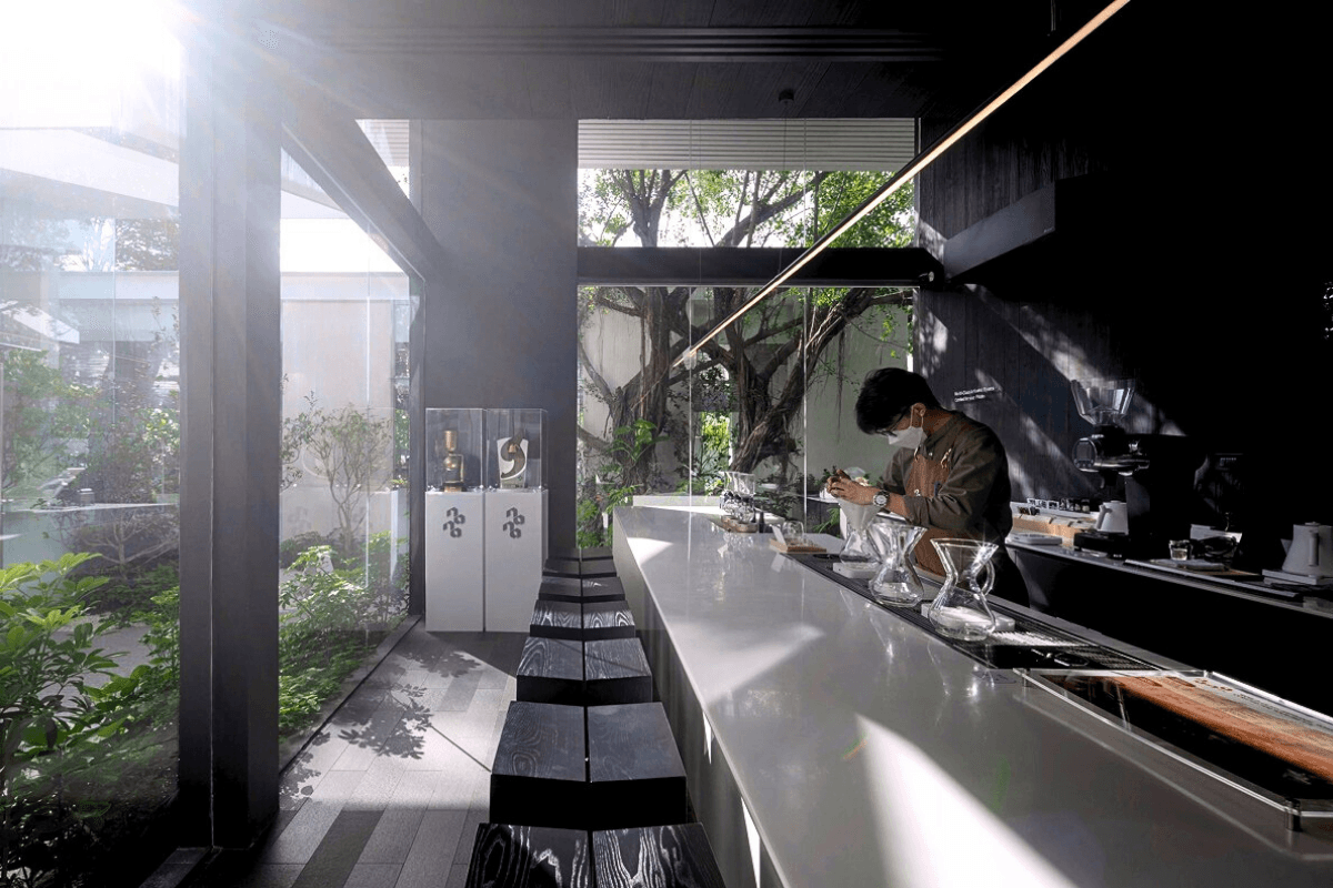 Кофейня «Nana Coffee Roasters», спроектированная бюроIDIN Architects, расположена в густонаселенном районе Бангна, Бангкок. Её основная цель — не ошеломить посетителя, а перенести его из городской суеты в спокойное и гармоничное пространство, где в центре внимания оказываются природа и сам кофе. Кофейня «Nana Coffee Roasters», спроектированная бюроIDIN Architects, расположена в густонаселенном районе Бангна, Бангкок. Её основная цель — не ошеломить посетителя, а перенести его из городской суеты в спокойное и гармоничное пространство, где в центре внимания оказываются природа и сам кофе.